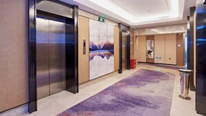 Un moderno vestíbulo de hotel con piso de mármol, un gran mural en la pared y un par de ascensores.