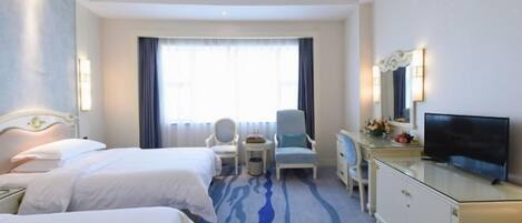 A hotel room with two beds, a desk with a TV, a chair, and a small table with flowers.