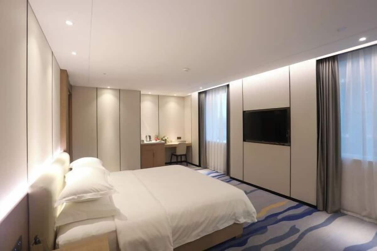 A modern hotel room with a bed, a desk, a chair, and a TV.