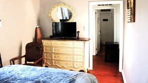 A bedroom with a bed, dresser, mirror, and a door leading to another room. - 1 Bedroom Suite upstairs (NEW ORLEANS)
