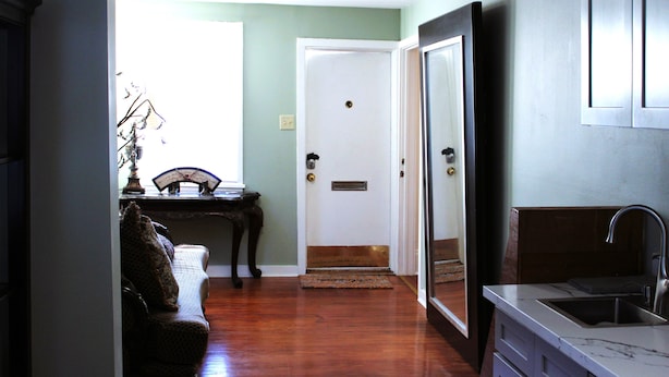 A hallway with a wooden floor, a door, a small table with a lamp, and a kitchen area with a sink. - 2 Bedroom Suite on second floor (NEW ORLEANS)