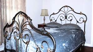 A bed with an ornate metal frame, a bedside table with a lamp, and a window with curtains. - 2 Bedroom Suite on second floor (NEW ORLEANS)