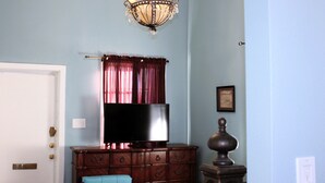 Una habitación con un aparador de madera, un televisor de pantalla plana, una araña y una puerta.