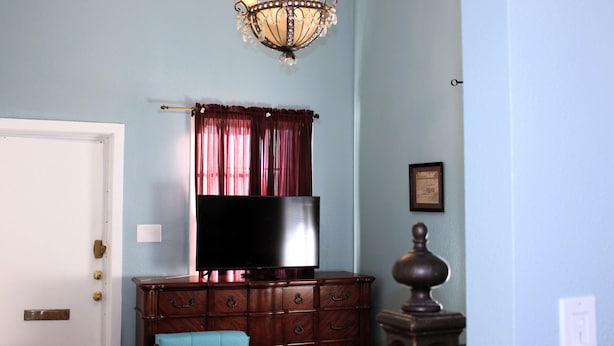 A room with a wooden dresser, a flat-screen TV, a chandelier, and a door.