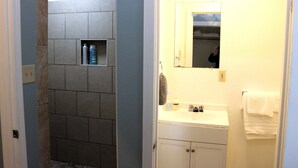 A bathroom with a tiled shower area, a sink with a mirror, and a towel rack.