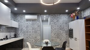 A compact kitchen with a glass-top dining table, white chairs, and patterned backsplash tiles. - Roma Vaticano Deluxe Apartment, just steps from the Metro and St. Peter's (Roma)