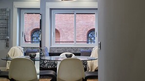A modern interior with a dining area, two chairs, a table, and a view of a brick building through large windows. - Roma Vaticano Deluxe Apartment, just steps from the Metro and St. Peter's (Roma)