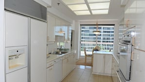 A modern kitchen with white cabinetry, a built-in oven, and a large window providing a view of the city. - The Pierre 507 by FGC (Longboat Key)