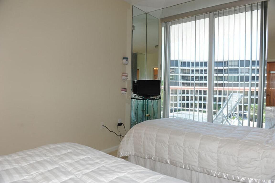 A hotel room with two beds, a large window with blinds, a mirror, and a television.