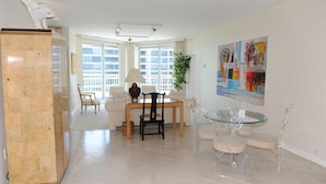 A spacious living room with a marble column, a dining area with a glass table and chairs, and a large window providing natural light. - The Pierre 507 by FGC (Longboat Key)