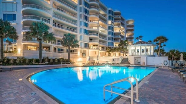 A hotel with a large swimming pool, multiple balconies, and palm trees. - The Pierre 507 by FGC (Longboat Key)