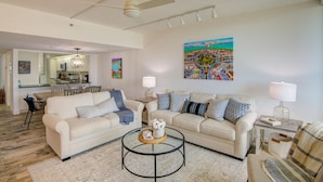 A spacious living room with two sofas, a coffee table, and a dining area with a chandelier. - Beachplace 3  - 302 by FGC (Longboat Key)