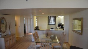 A spacious dining area with a glass-top table and wooden chairs, a kitchen in the background, and a large mirror on the wall. - Partial Beach View 2 Bedroom Condo (Longboat Key)
