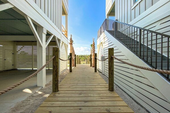 A wooden pathway leading to a building with a staircase and a railing.