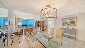 Een moderne woonkamer met een glazen eettafel, zachte zitplaatsen, een groot raam met uitzicht en een bijzondere bamboe kroonluchter.