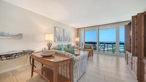 Amplia sala de estar con un gran ventanal con vistas al mar, un conjunto de sofás, una mesa de centro y un comedor con vistas.