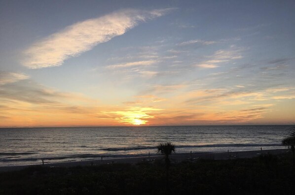 A sunset over the ocean with a beach in the foreground.
