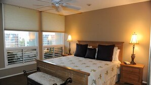 Une chambre à coucher avec un lit, des lampes de chevet, un banc et un ventilateur de plafond.