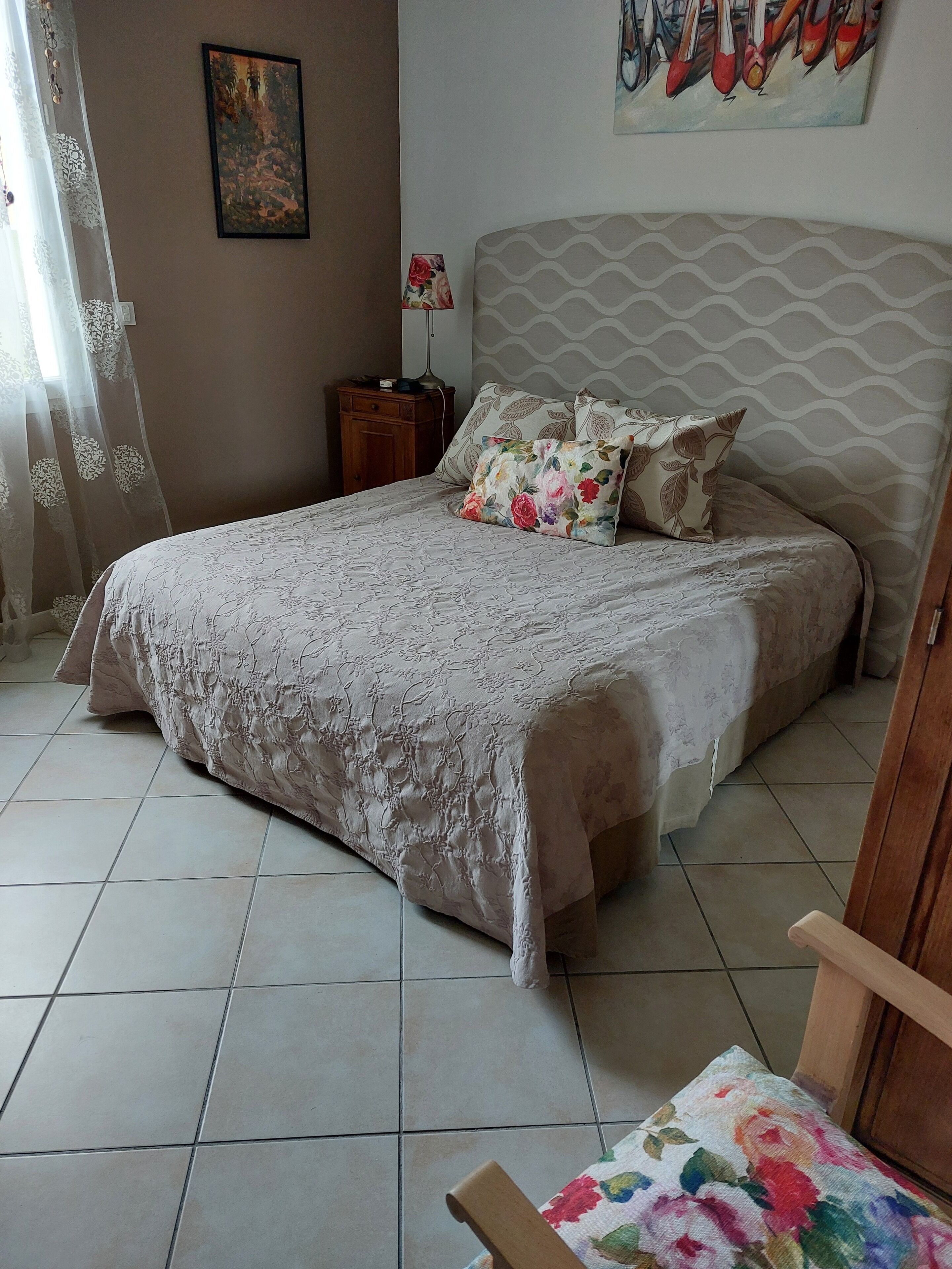 A neatly made bed with floral bedding, a patterned headboard, and a nightstand with a lamp.