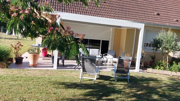 A covered patio with outdoor furniture, a garden with potted plants, and a house with a tiled roof. - Semi-detached house in the countryside garden covered terrace (Lahourcade)