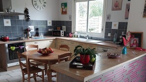 A modern kitchen with a central island, a dining table, and a large wall clock. - Semi-detached house in the countryside garden covered terrace (Lahourcade)
