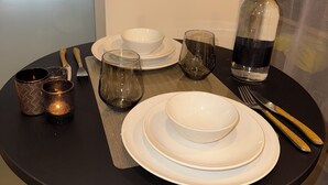 A dining table set with white plates, bowls, glasses, and cutlery. There is a bottle and two candles on the table. - STUDIO COCON DeSIGN (Saint-André-les-Alpes)