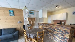 Un espacio habitable compacto con zona de comedor, sofá, pequeña cocina y una pared decorativa con obras de arte.