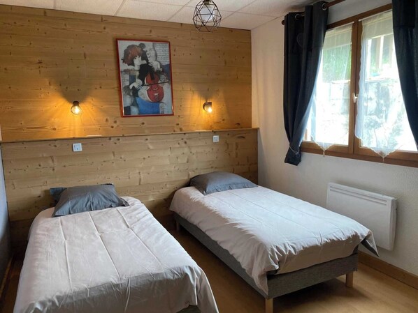 Et værelse med to enkeltsenge, et træhovedgærde, et maleri, to vægmonterede lamper, et vindue med gardiner og en radiator.