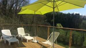 Una terraza de madera con sillones de descanso blancos y un paraguas amarillo.