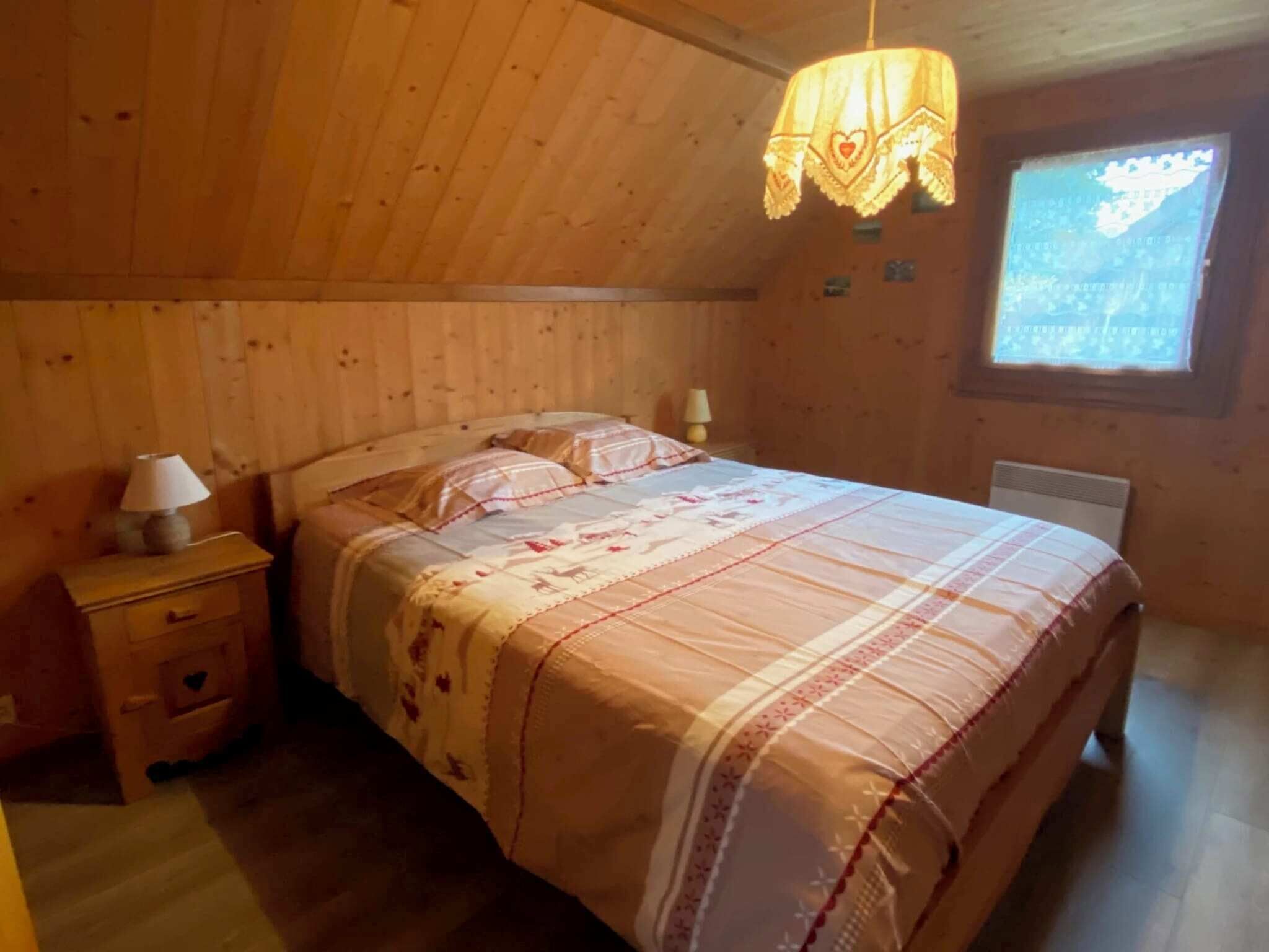 Un dormitorio acogedor con techo de madera, una cama con colcha estampada, una mesita de noche con lámpara y un ventanal con vistas.