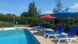 A swimming pool with blue water, surrounded by white lounge chairs and blue umbrellas. - Chalet des planchettes le lynx (Marigny)