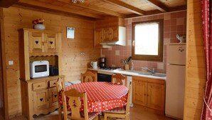 A wooden cabin kitchen with a dining table, cabinets, a microwave, a stove, and a refrigerator. - Chalet des planchettes le lynx (Marigny)