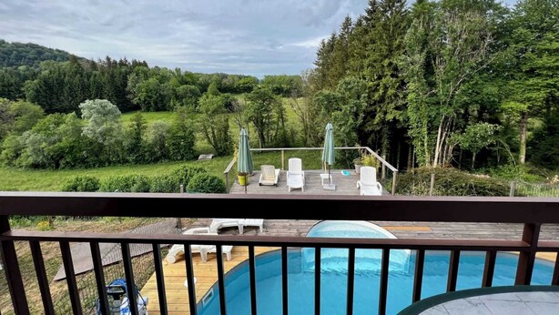 Una terraza de madera con piscina, rodeada de vegetación exuberante y árboles.