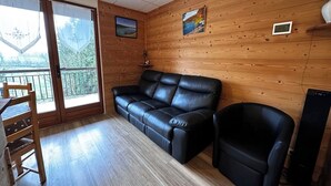 Una habitación con paneles de madera, un sofá de cuero negro, una mesa de comedor de madera con sillas y una pequeña silla negra.