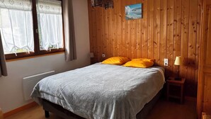 Un dormitorio con una cama, dos almohadas, una ventana con cortinas, un cuadro en la pared y una lámpara de noche.