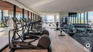 A modern gym with treadmills, stationary bikes, and weight machines, featuring large windows and a city view.