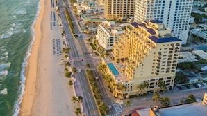 Ein Luftbild eines an der Küste gelegenen Hotels mit mehreren Hochhäusern, einem Strand und einer gepflegten Straße.