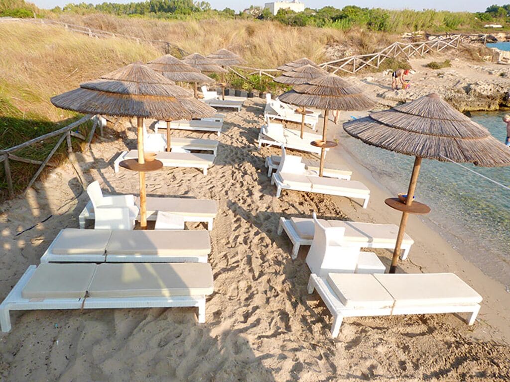 Ein Strand mit weißen Liegestühlen und reetgedeckten Sonnenschirmen.