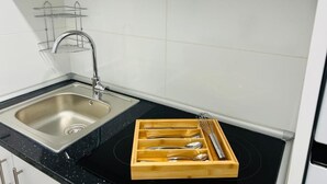 Ett kök med en diskho i rostfritt stål, ett träställ för köksredskap och en svart spishäll.