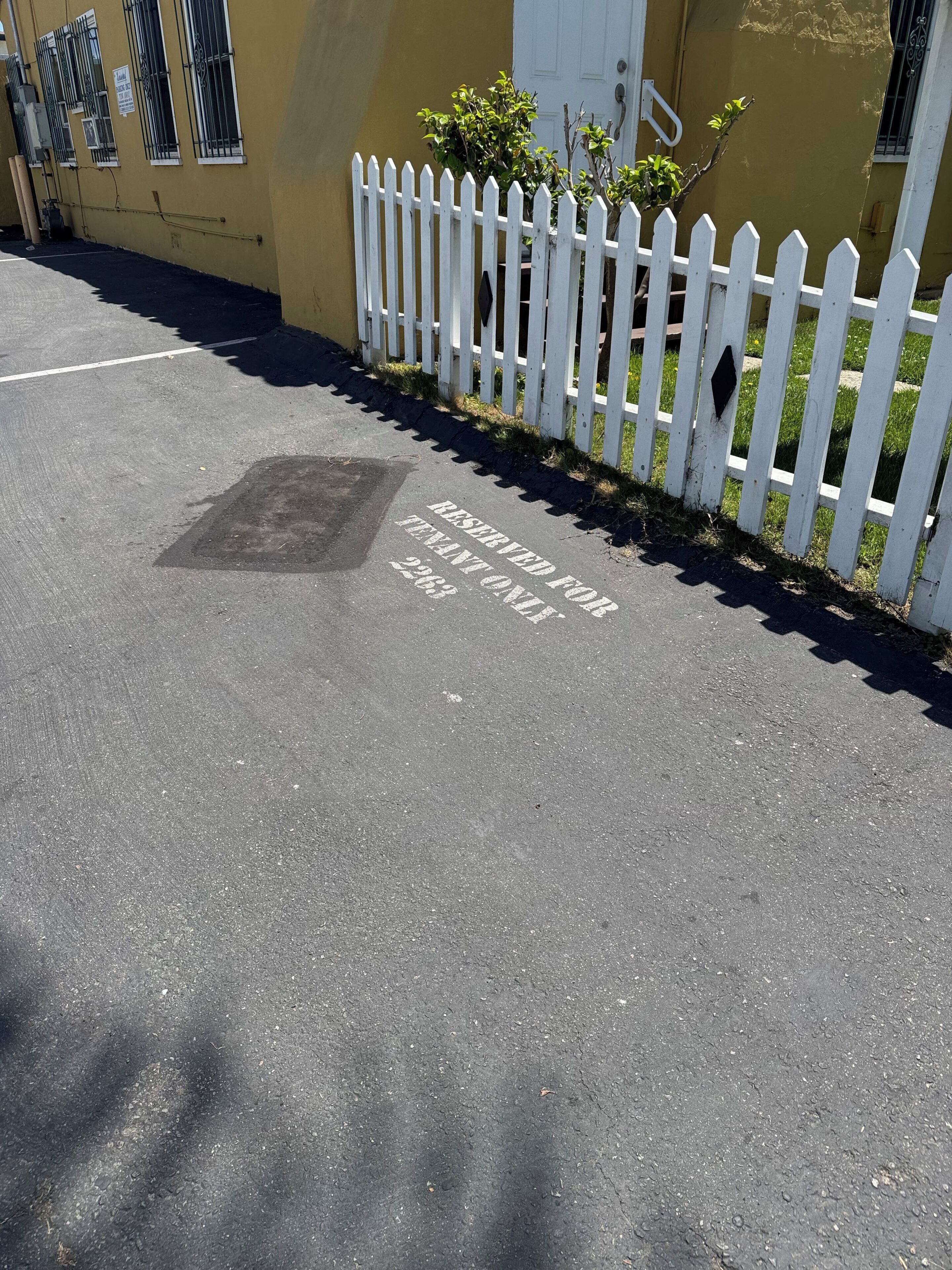 A parking area with a white picket fence and a yellow building in the background.