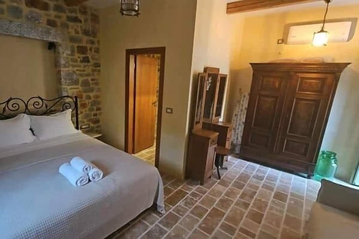 Ein Schlafzimmer mit Steinwand, einem Bett mit gerollten Handtüchern, einem Holzschrank und einem Fliesenboden.