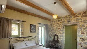 Un dormitori amb llit, una tauleta de nit, un armari, un mirall, una paret de pedra, un sostre de fusta i una porta verda.