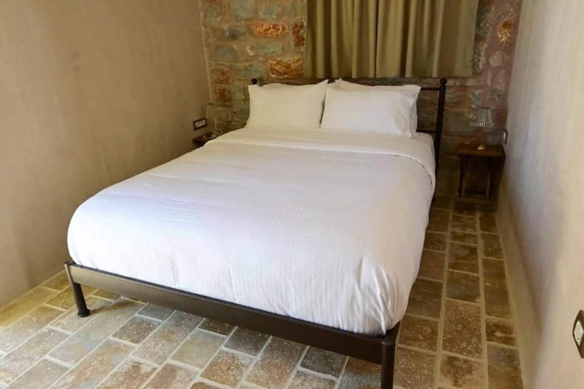 Ein Bett mit weißer Bettwäsche in einem Zimmer mit Steinwänden und Fliesenboden.