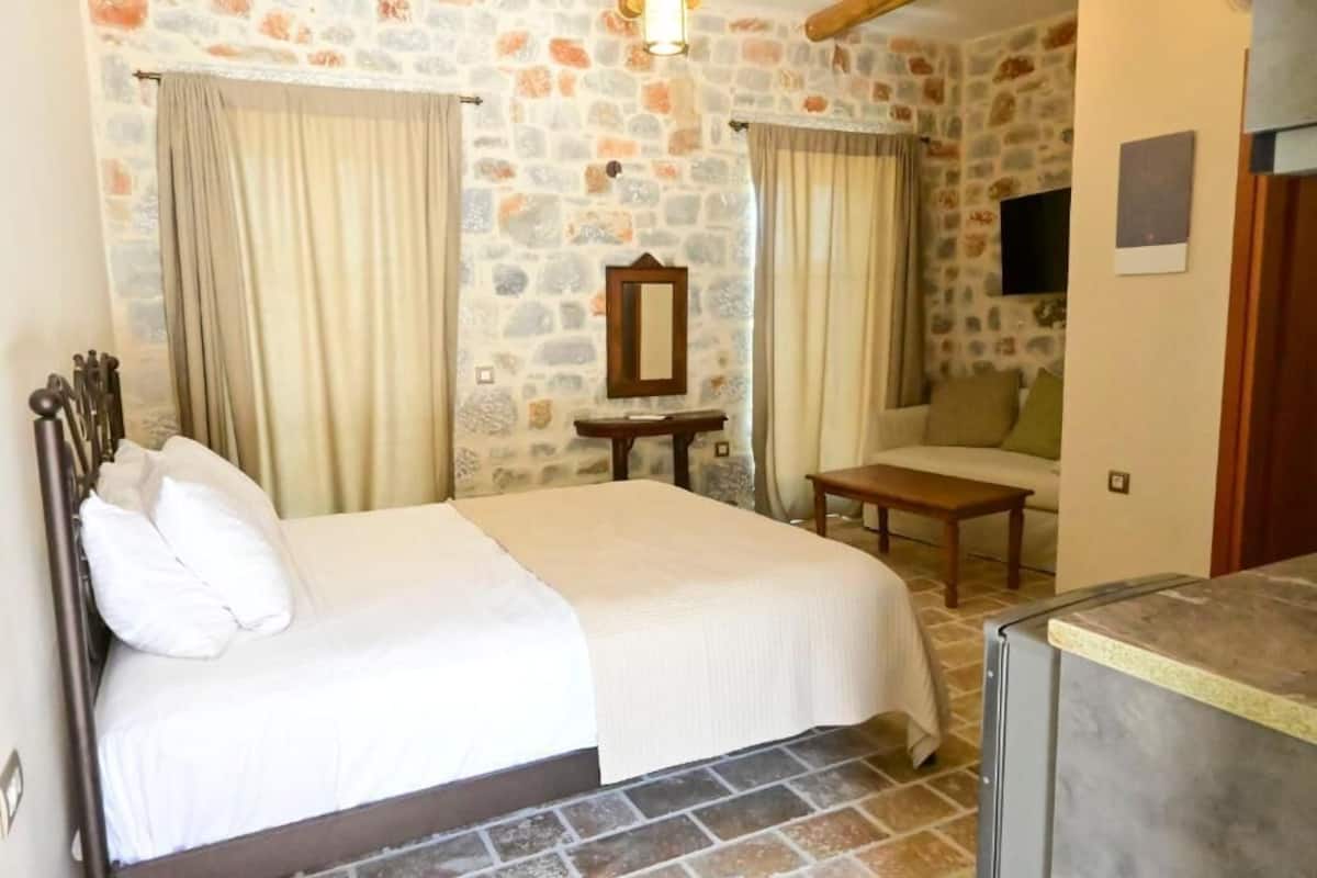 Ein Schlafzimmer mit Steinwand, einem Bett mit weißer Bettwäsche, einem hölzernen Nachttisch, einem kleinen Tisch und einem an der Wand befestigten Fernseher.