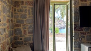 Habitació de parets de pedra amb sofà, televisió i porta que dóna a l'exterior.