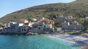 Un poble costaner amb edificis de pedra, una platja i un turó al fons.