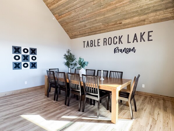 A dining area with a wooden table and chairs, a wall-mounted sign reading "TABLE ROCK LAKE Branson," and a geometric wall decoration.