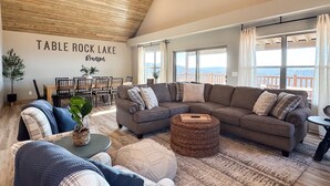 A spacious living room with a large sectional sofa, a dining table with chairs, and a view of the lake.