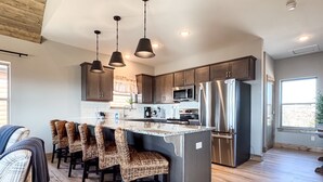 A modern kitchen with a central island, bar stools, stainless steel appliances, and pendant lighting.
