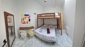 Una habitación pequeña y bien iluminada con una cama litera, un escritorio, dos sillas, un espejo y un cuadro abstracto colorido en la pared.